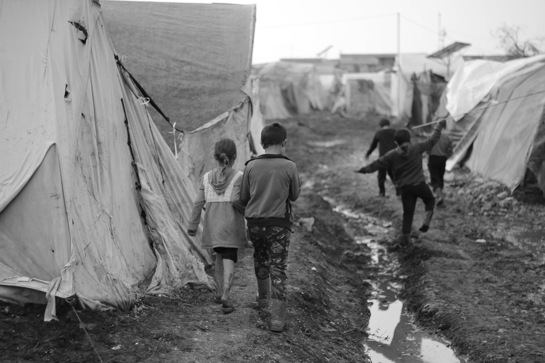 a black and white photo of children walking through a refugee camp